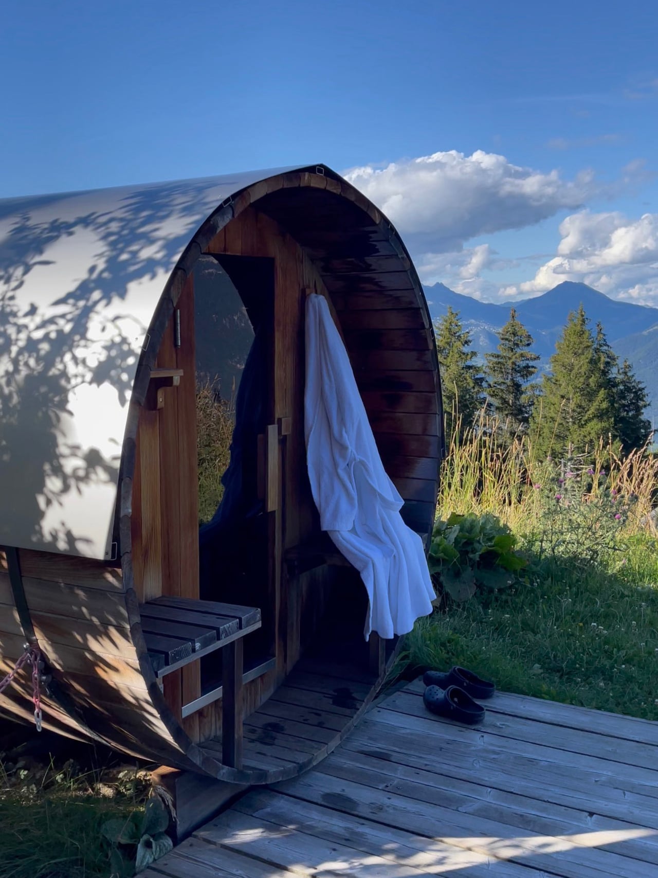 A barrel sauna on the deck with mountain views and a robe hanging at the door