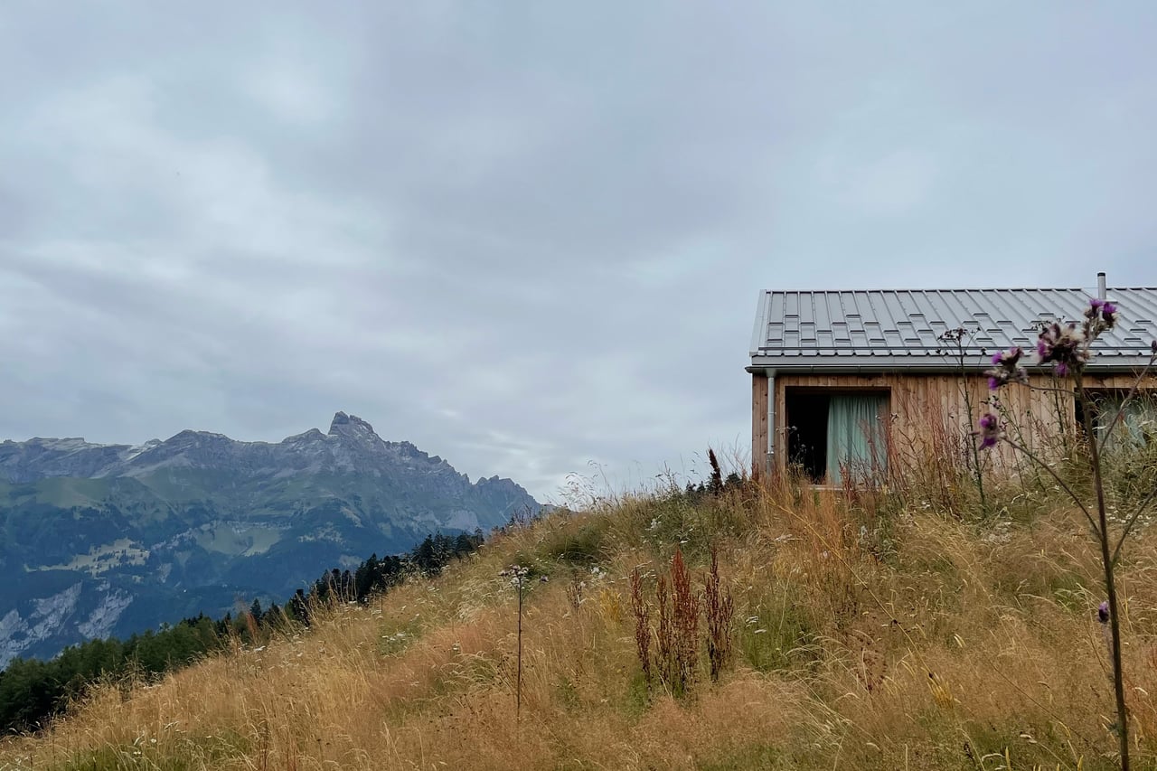 A timber Whitepod chalet perched on the meadow slope with the Dents-du-Midi in the distance