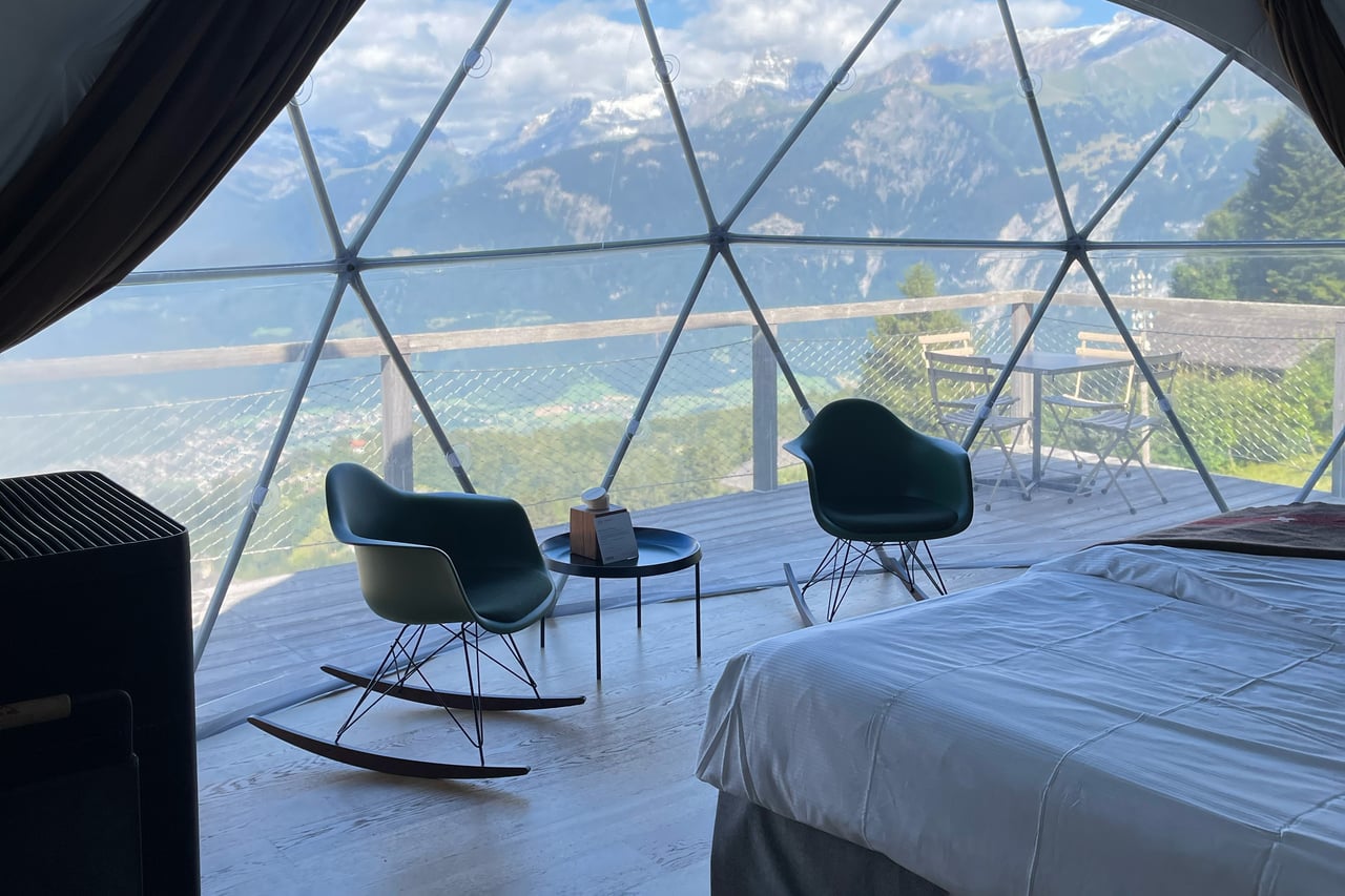 Inside a Whitepod Family Pod — green rocking chairs, a bed and floor-to-ceiling mountain views through the geodesic shell