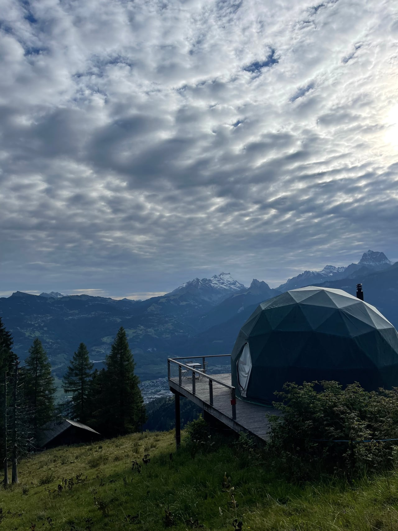 A Whitepod geodesic pod on its deck at dusk under a mackerel sky, the Dents-du-Midi beyond